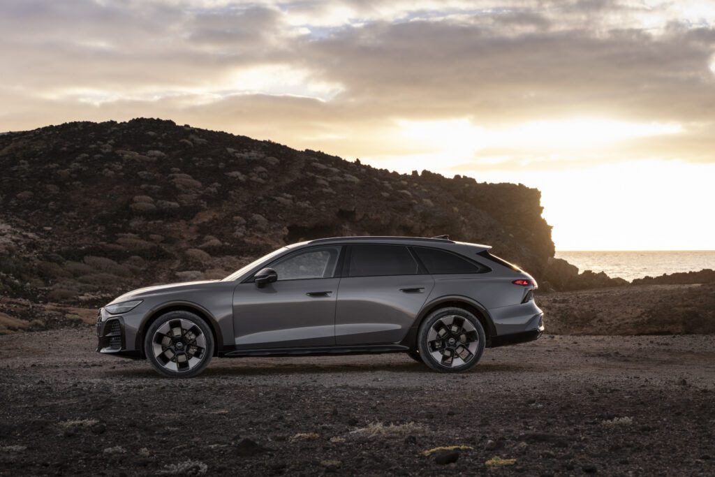 Side silhouette of the Audi A6 allroad (plateau grey metallic) at low sun along a rugged coastline.